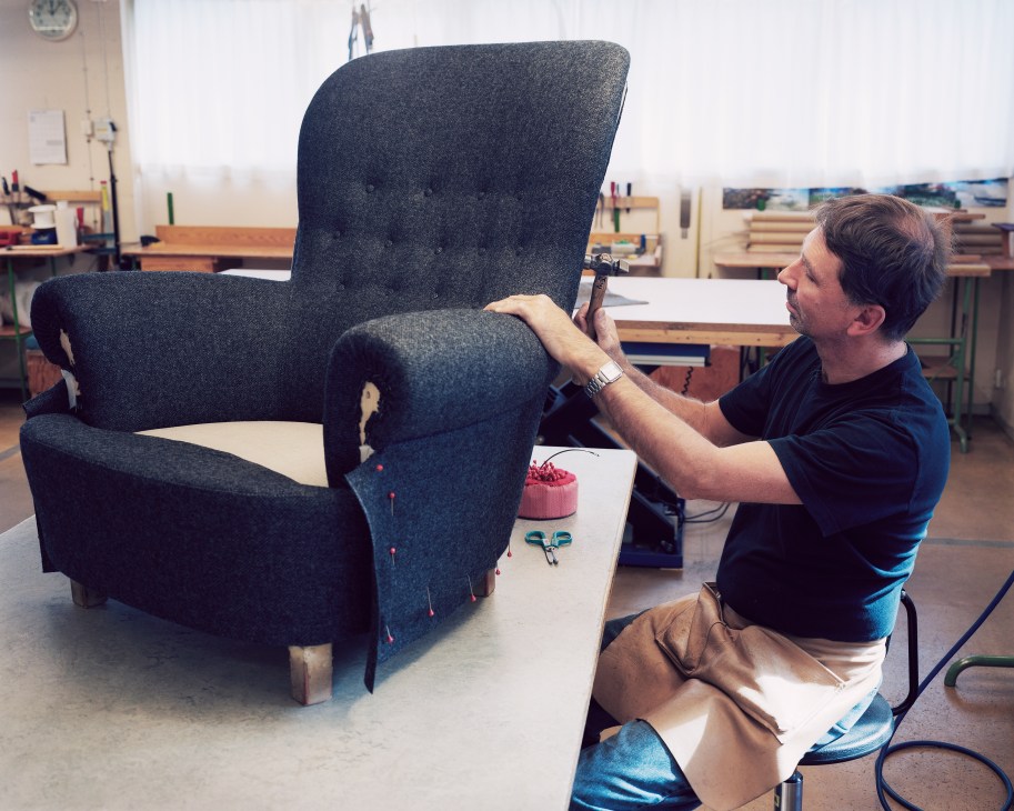Craftsman working on upholstering a dark grey Jättepaddan armchair in a workshop.