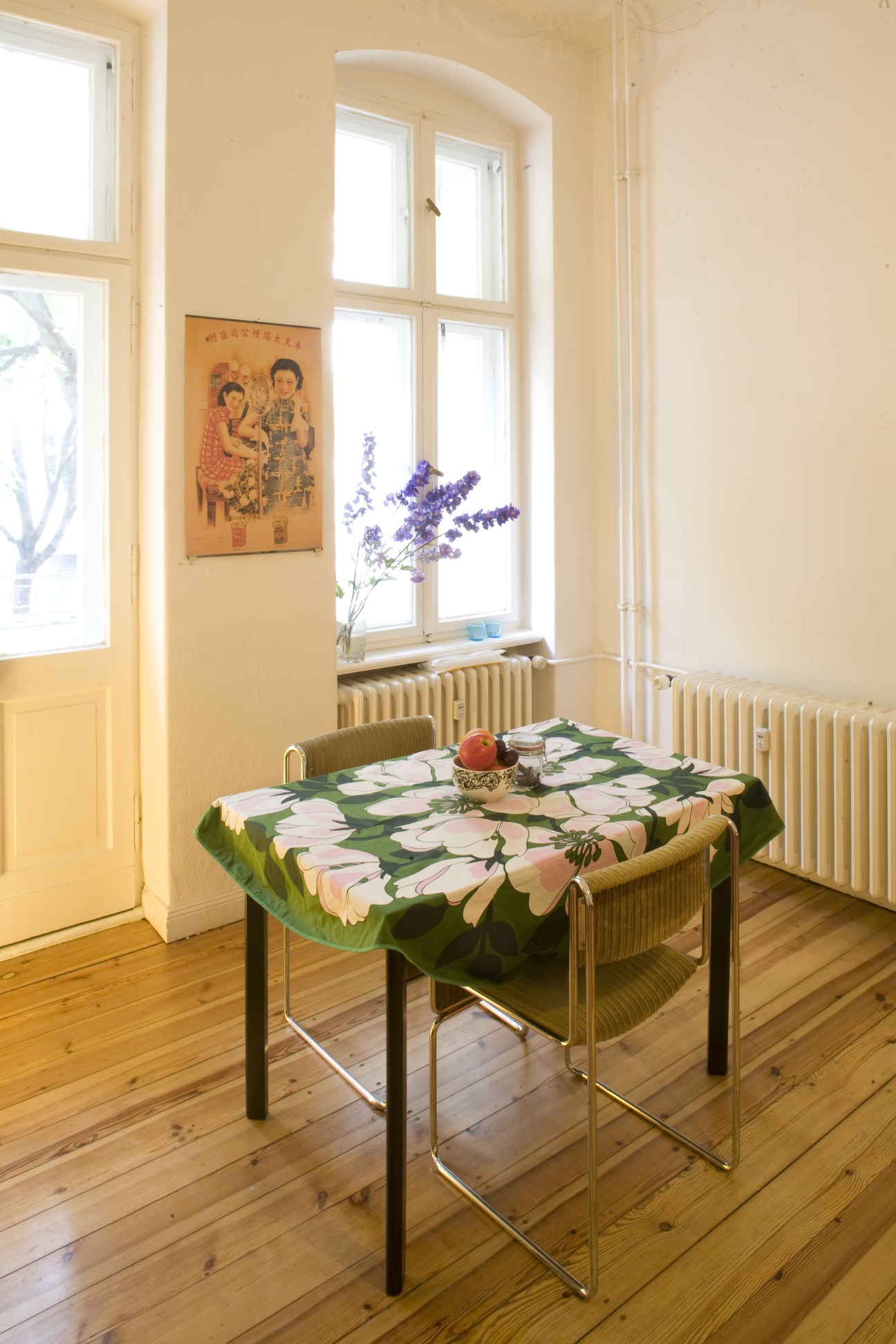 Bright living room with yellow walls, large arched windows, wooden floorboards, and a table with green floral tablecloth.