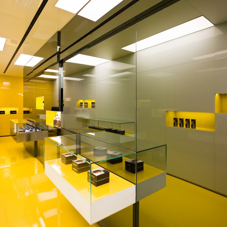 Interior of Pomme Sucre bakery with yellow and white display cases, glass partitions and skylights.