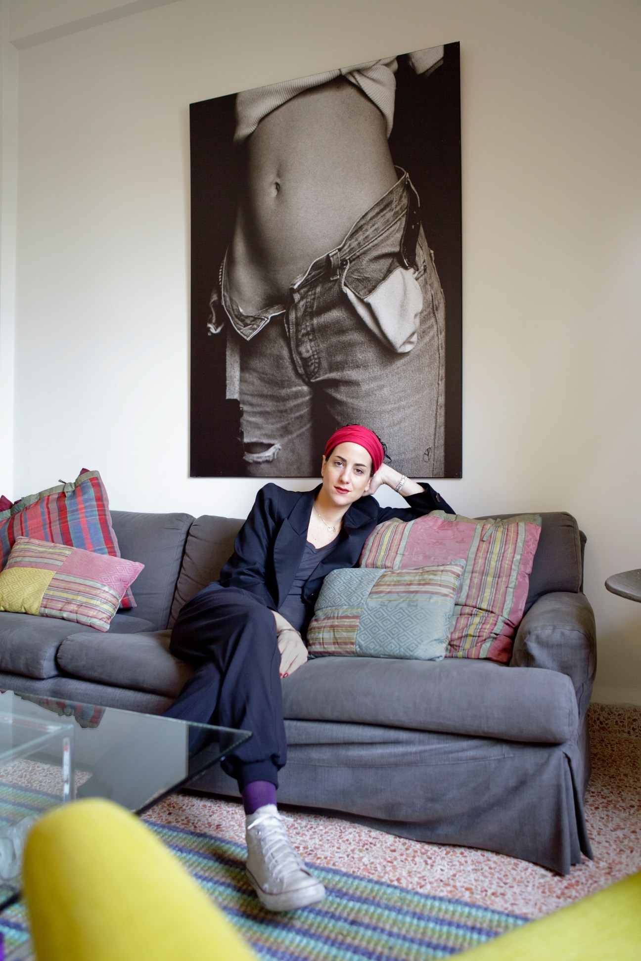 Caline Chidiac sits on a gray sofa wearing a navy blazer and pink headband in her Mar Mikhael apartment.