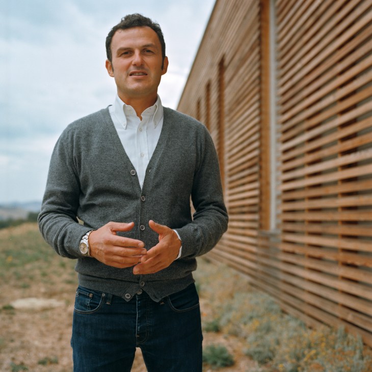 Pastificio owner Massimo Mancini standing outdoors in a gray cardigan next to a wooden building.