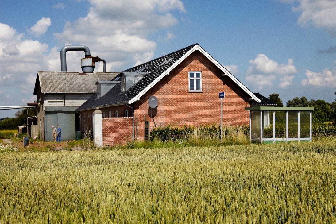 Red brick workshop building with metal chimney in rural field setting