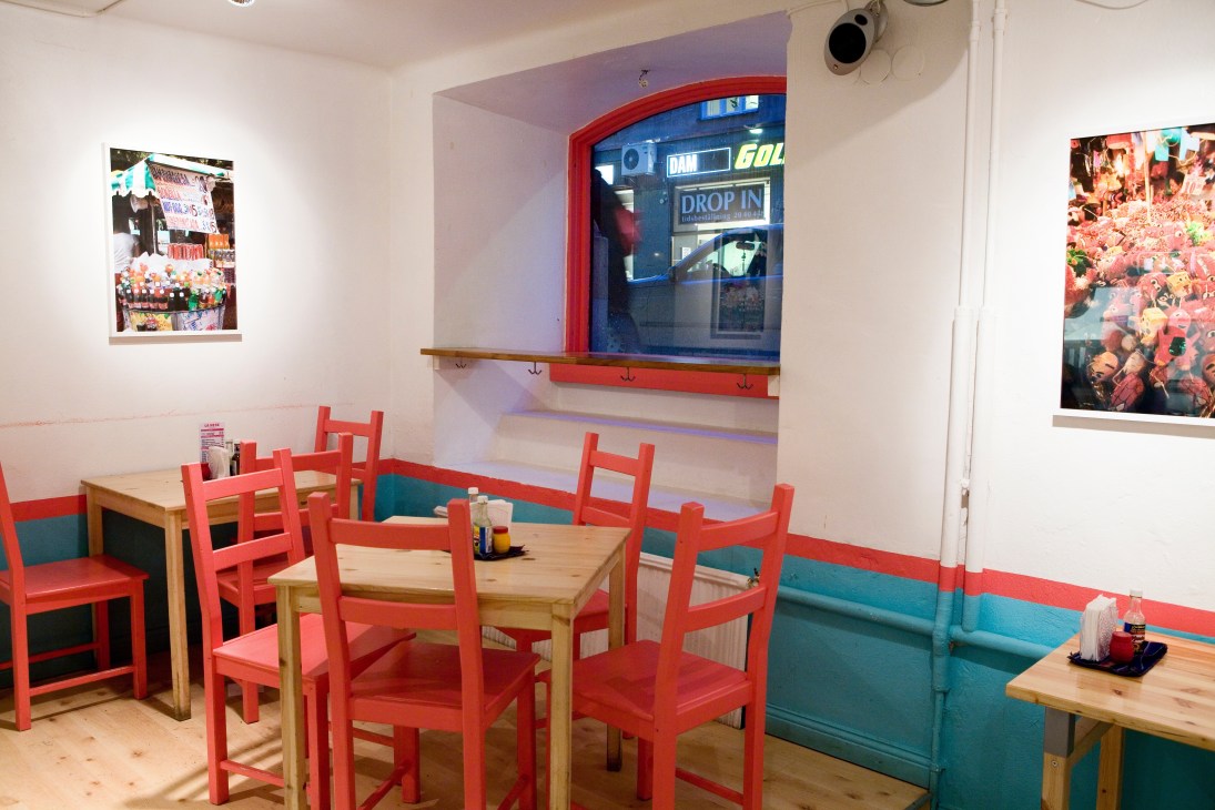 Interior of La Neta restaurant with red chairs, wooden tables, and teal banquette seating.
