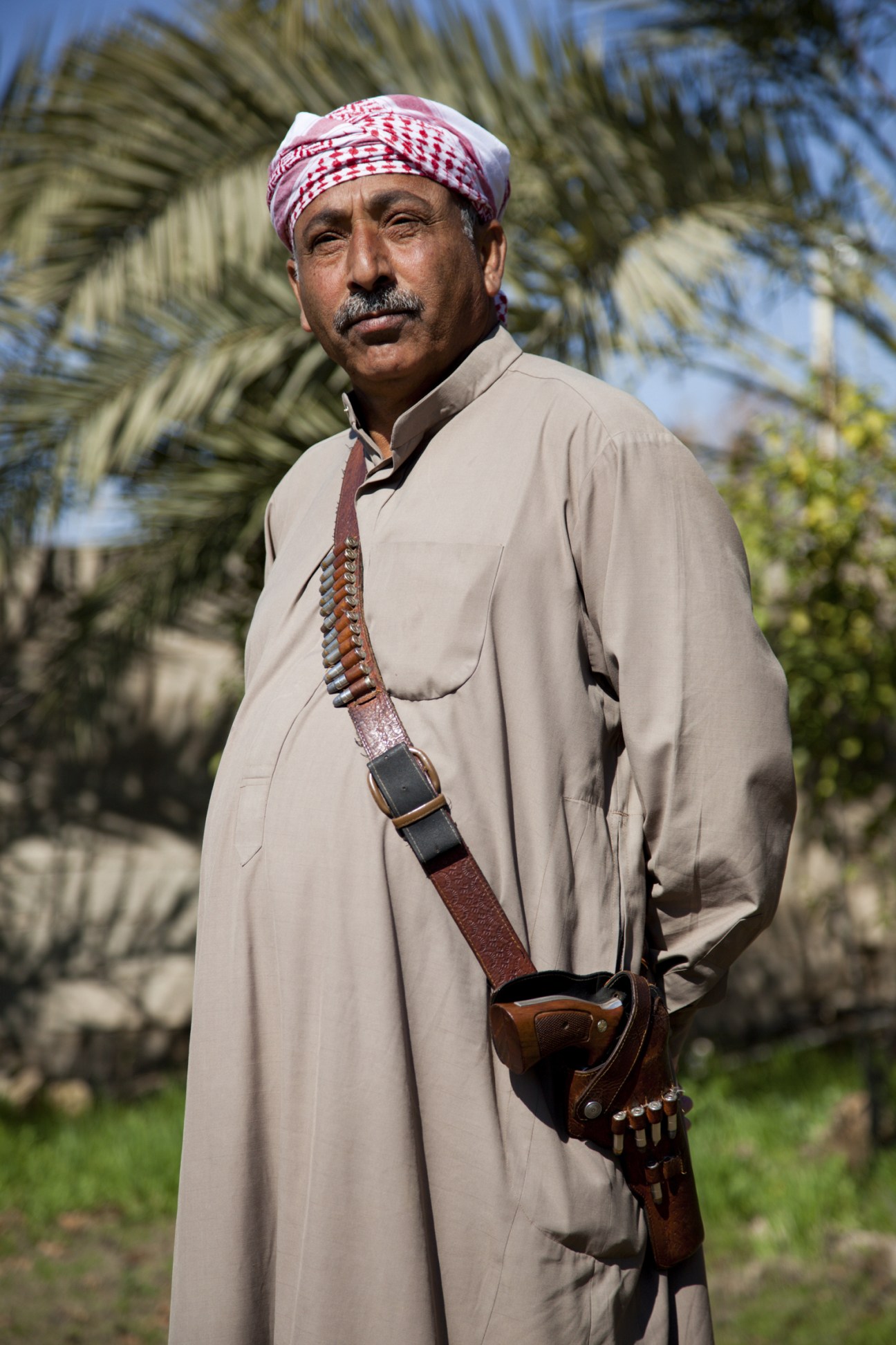 General Mustafa Kamil in traditional dress and armed uniform standing among palm trees.