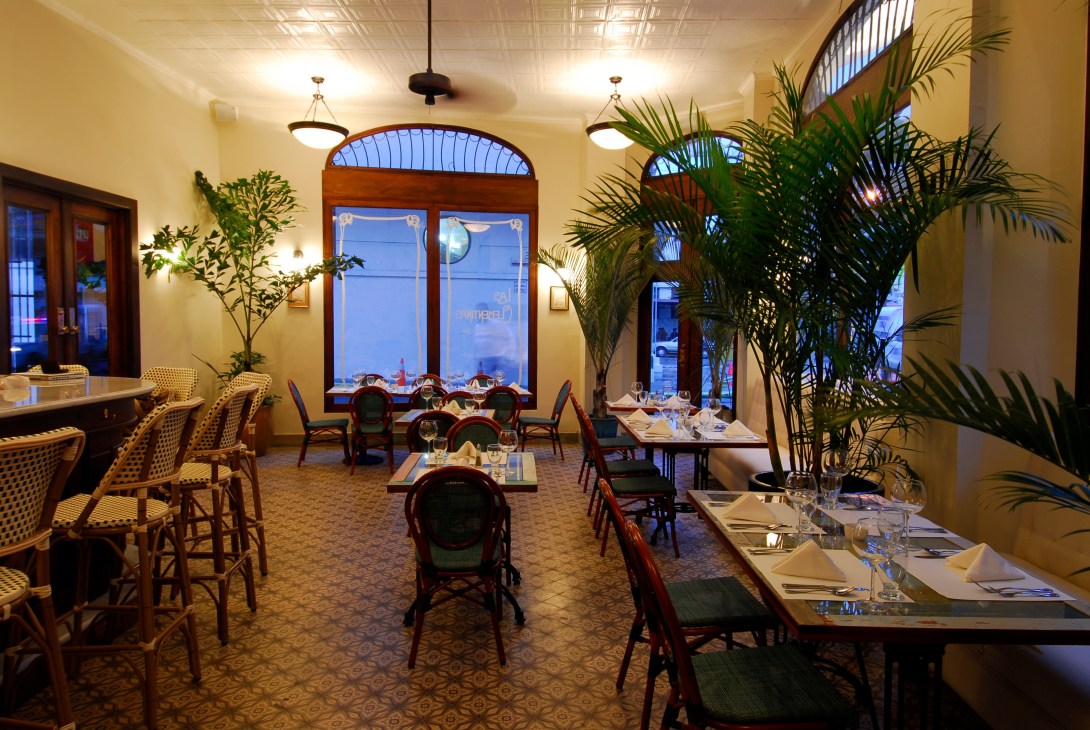 Interior of Las Clementinas restaurant with elegant dining tables, woven chairs, potted plants, and arched windows overlooking Panama City.