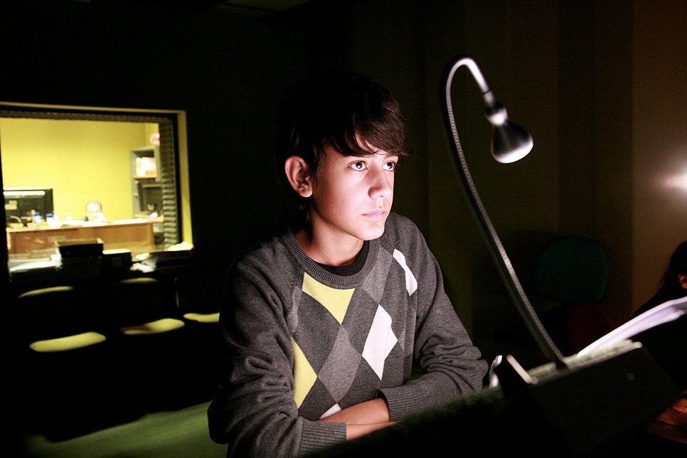 Leonardo Caneva, an Italian voice actor, sits at a desk in a recording studio with a microphone and script.