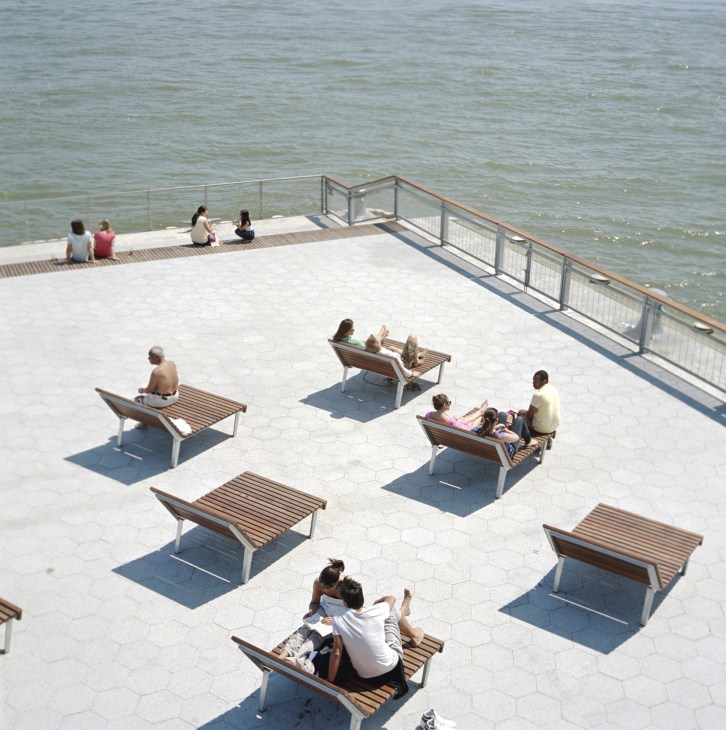 People relax on wooden benches at Pier 15 waterfront with metal railings and water visible in background.