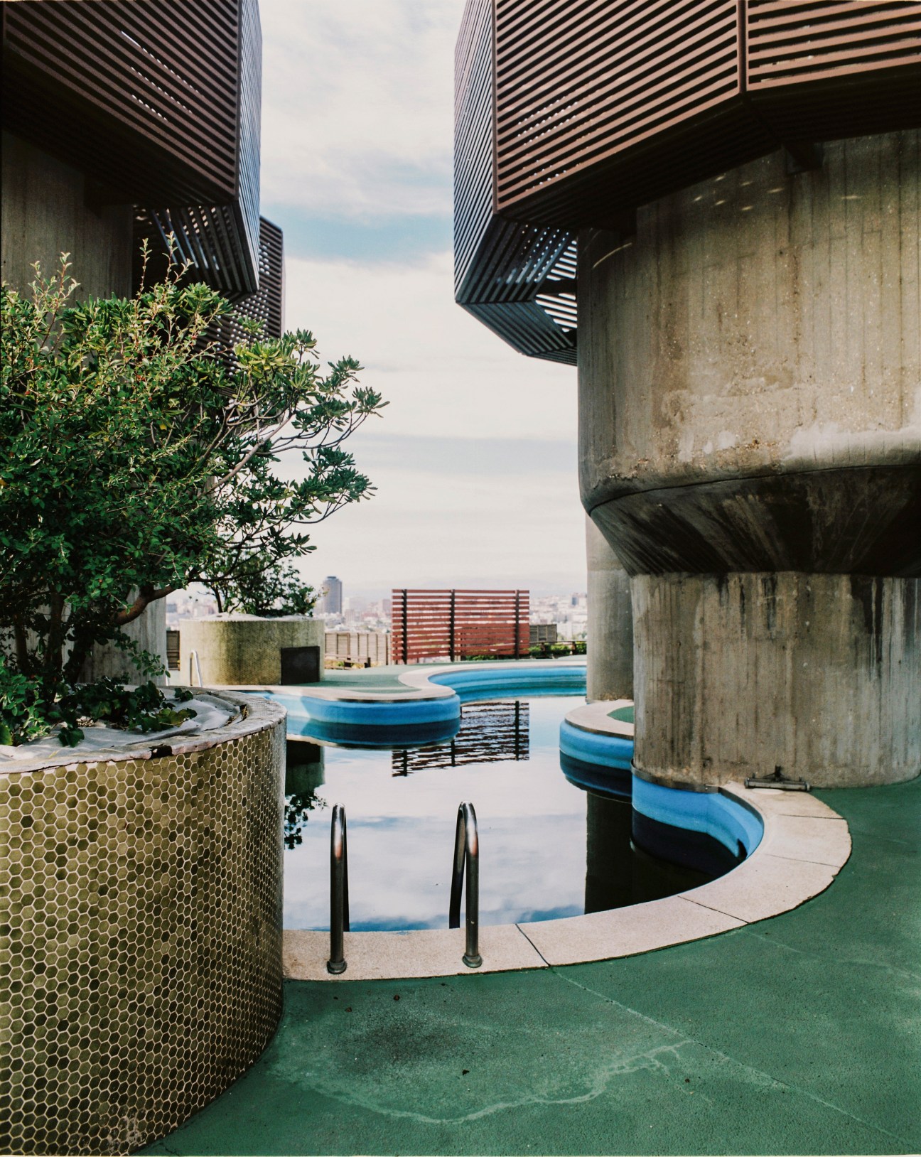 Rooftop pool surrounded by modernist concrete structures and striped metal screens overlooking Madrid cityscape.