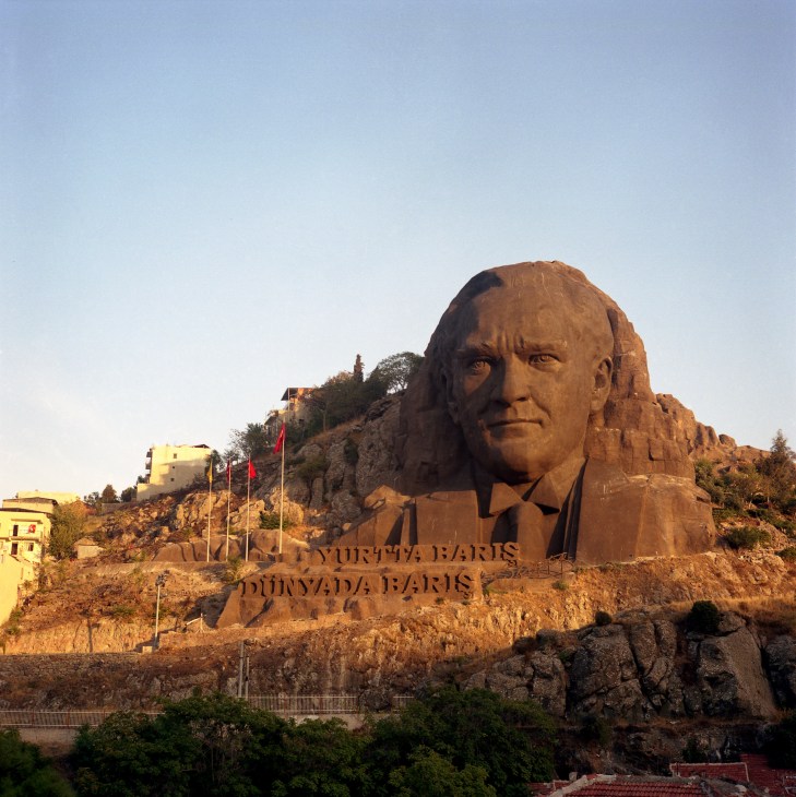 Large stone statue of Mustafa Kemal Atatürk carved into a hillside with Turkish flags at its base.