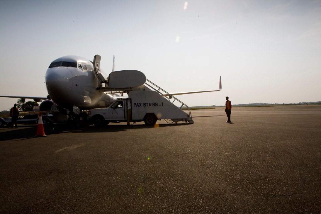 A Kenya Airways passenger aircraft parked on an airport tarmac with passenger stairs and ground vehicles nearby.