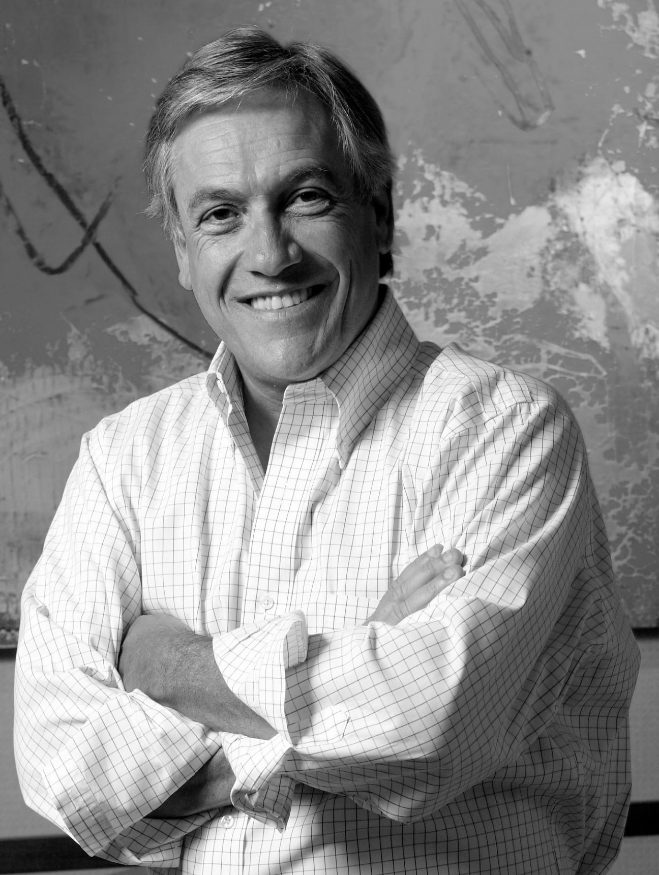 Portrait of Sebastián Piñera, Chilean president, smiling in a white checkered shirt against a textured background.