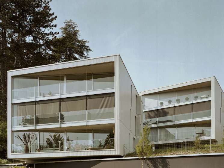Two modern white wooden apartment blocks with large windows overlooking Meilen Lake in Zurich, designed by e2a architects.