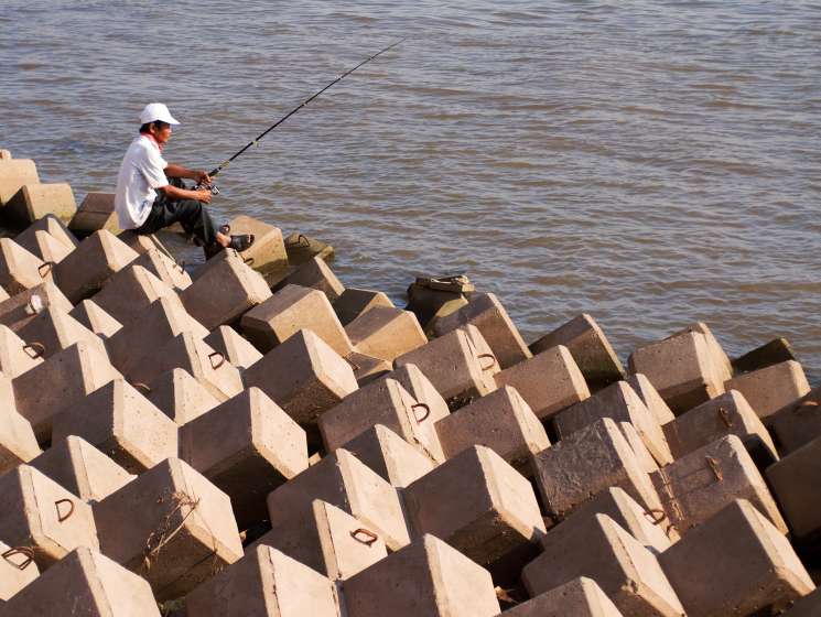Fisherman casting a line from newly installed concrete flood barriers along Phnom Penh's riverfront.