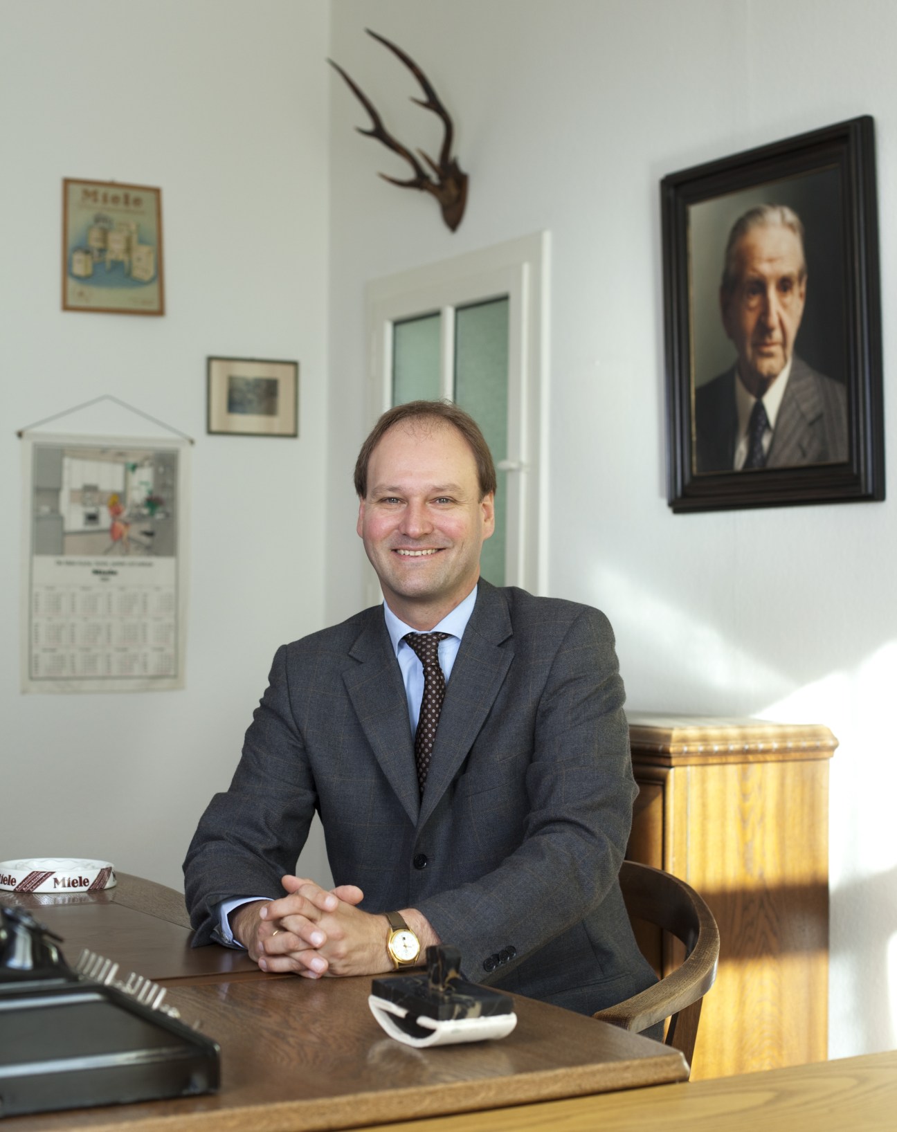 Dr Markus Miele, managing director and co-proprietor of Miele, sits at his desk in an office displaying company history and heritage items.