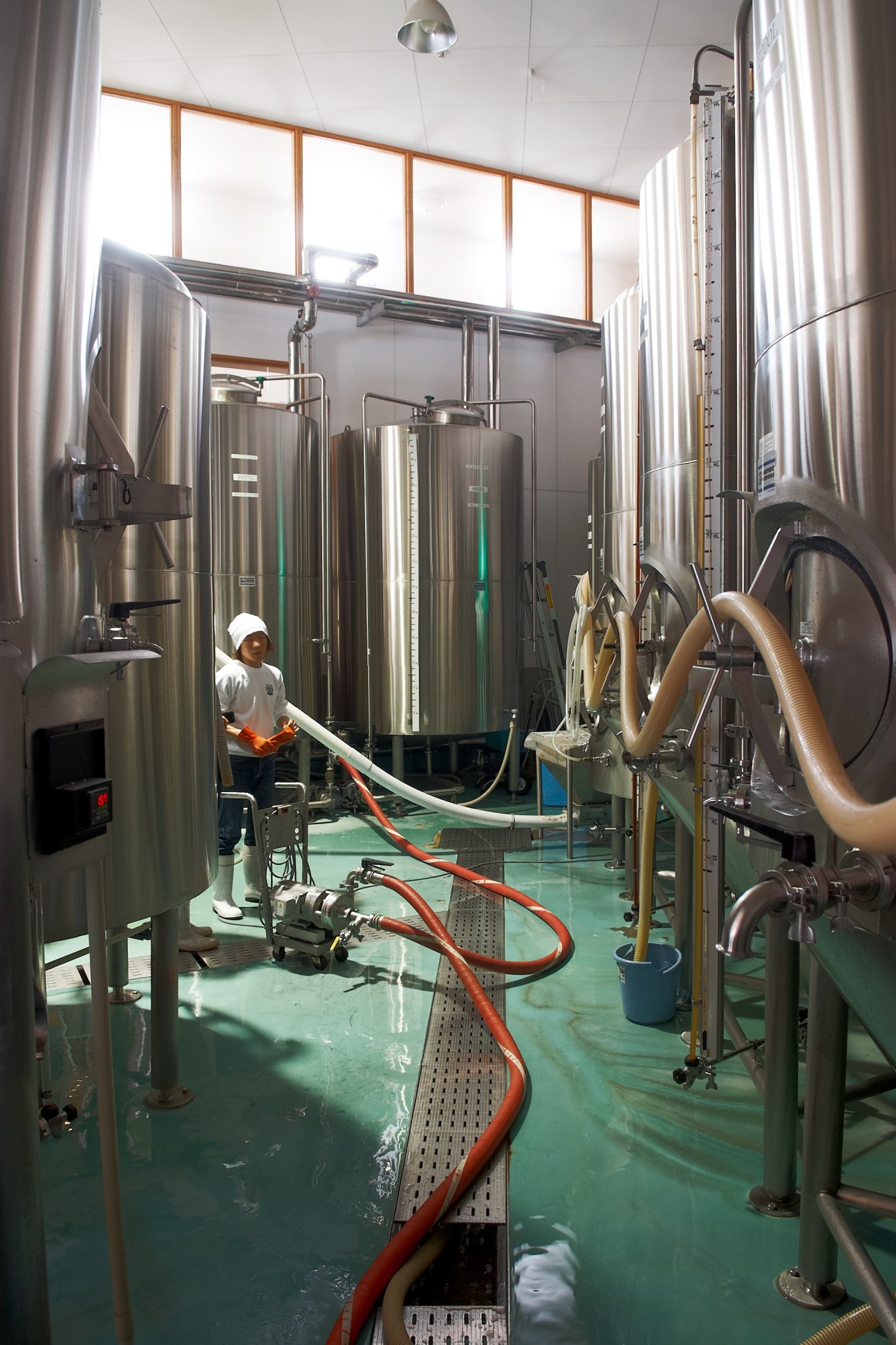 A brewer works inside Swan Lake brewery's fermentation room with large stainless steel tanks and equipment.