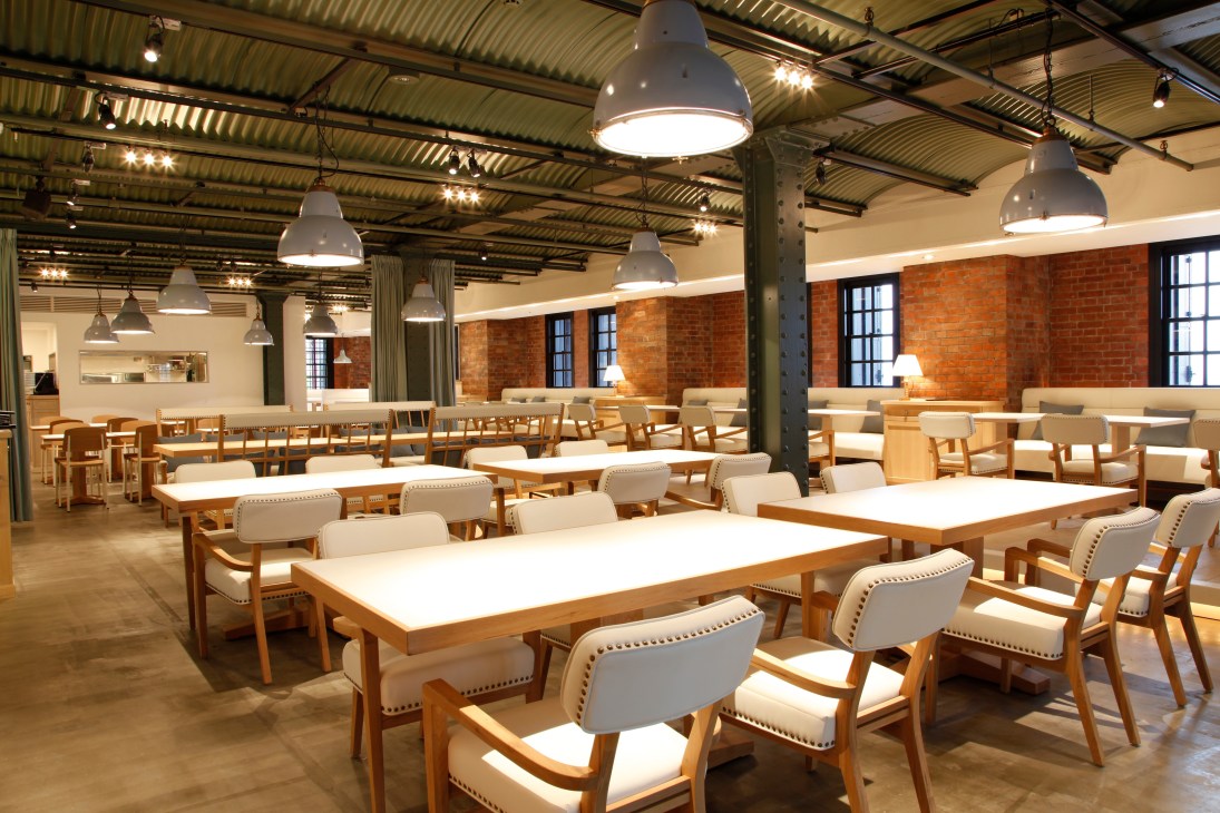 Interior of Bills restaurant in Yokohama with wooden tables, cream chairs, industrial ceiling, and exposed brick walls.