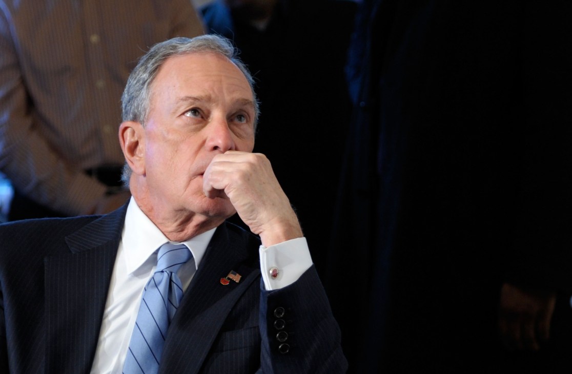 Michael Bloomberg in formal business attire with hand near his face in a thoughtful pose.