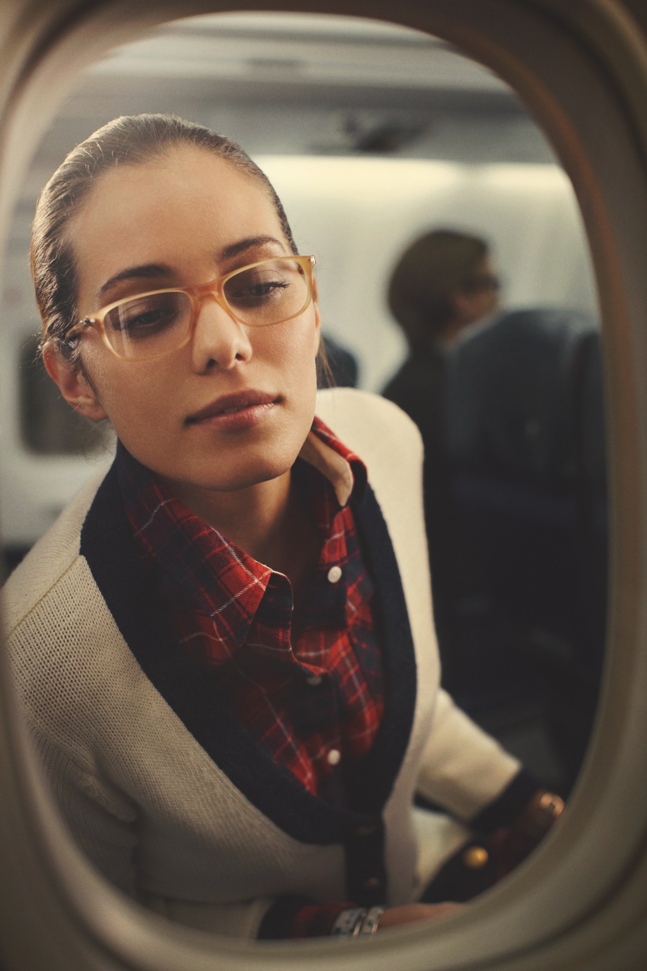 Woman wearing Persol glasses and cardigan by Macphee on an airplane next to window.