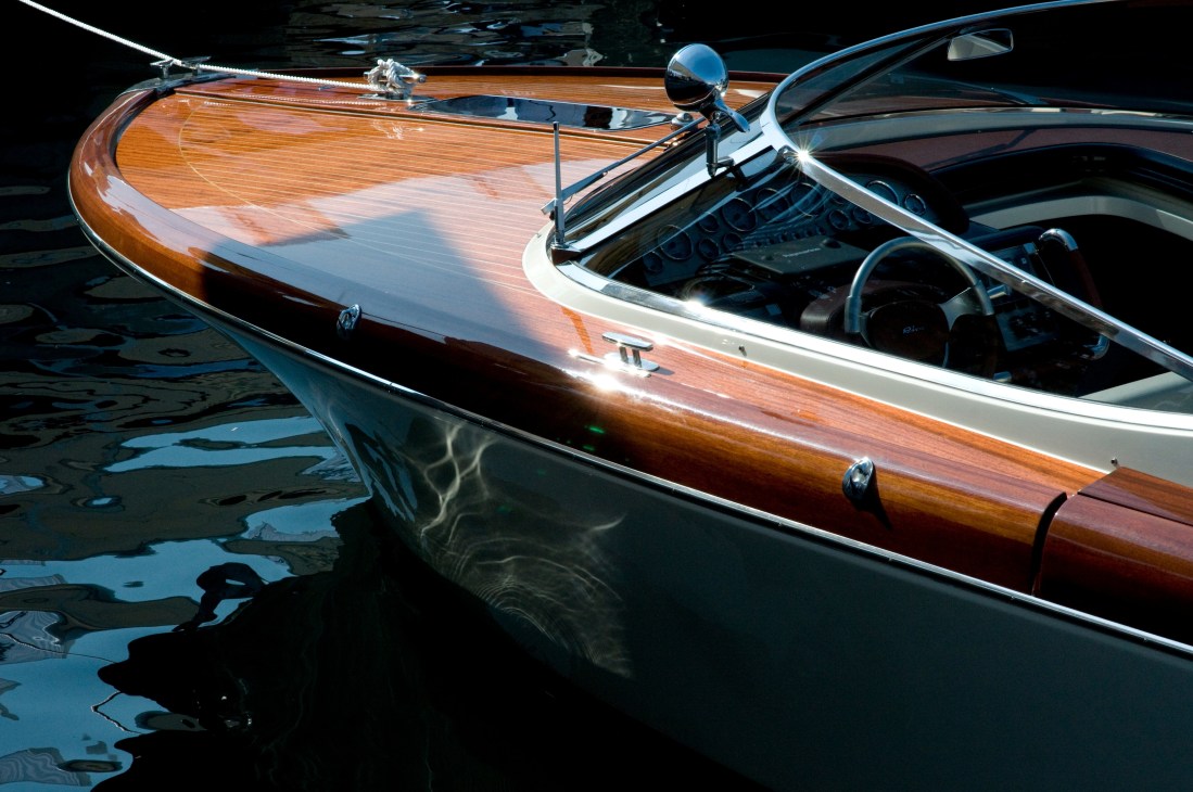 Classic Riva runabout with polished mahogany hull and white trim moored in water.