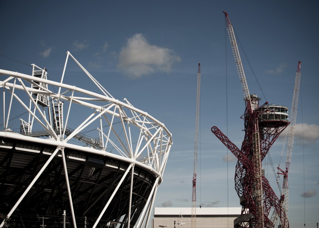 White steel framework of Olympic stadium under construction with red cranes against blue sky