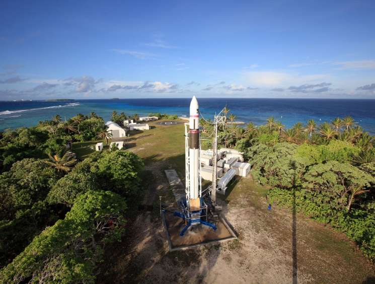 Aerial view of a white rocket on a launch pad surrounded by tropical vegetation and ocean.