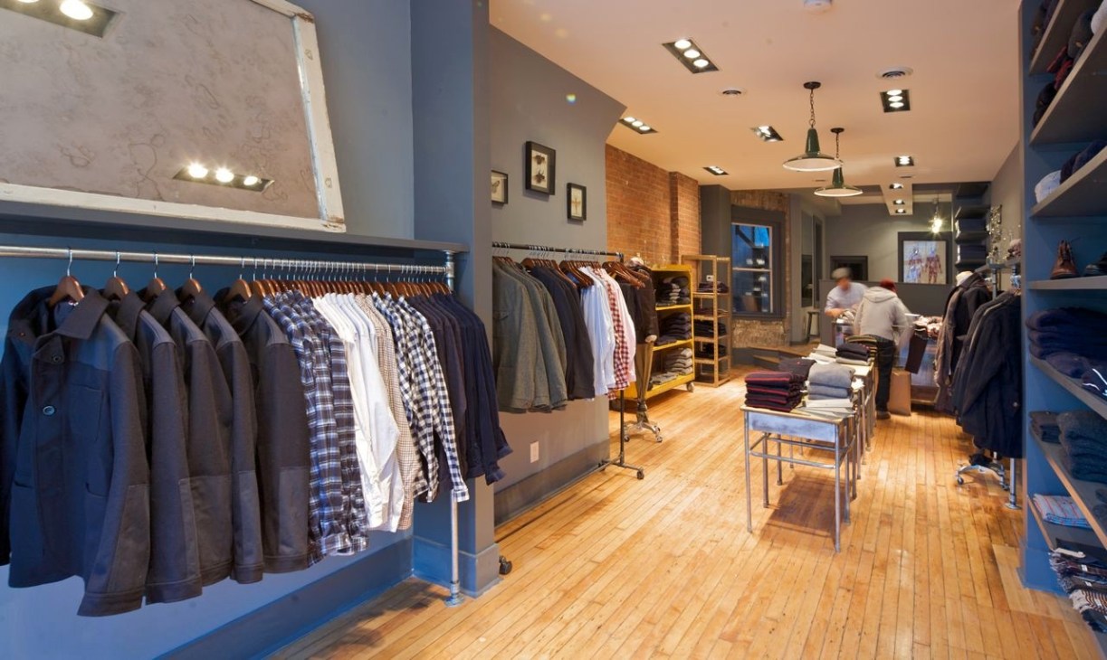 Interior of Oliver Spencer boutique with clothing racks and brick walls.