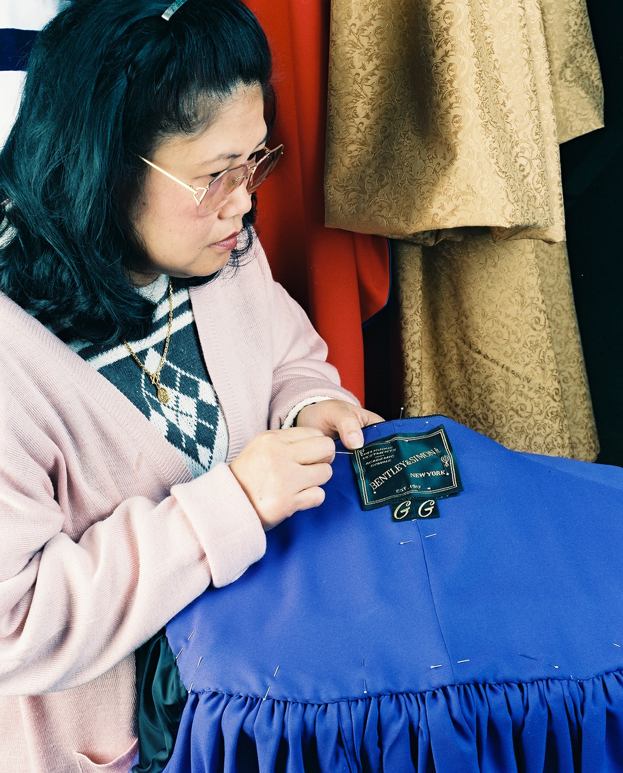 Woman examining a blue judicial robe with Bentley & Simon label from New York.