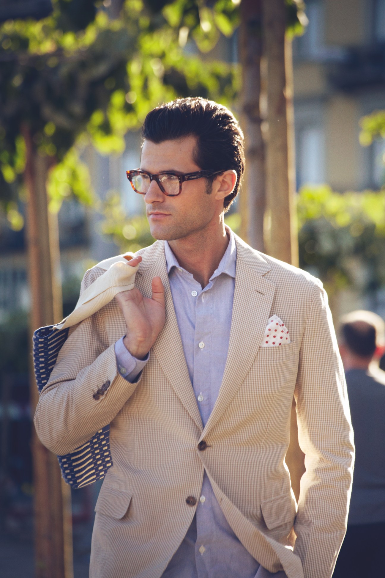 Man in beige Brioni jacket and light blue Glanshirt wearing Claire Goldsmith glasses, holding Johanna Gullichsen bag over shoulder.