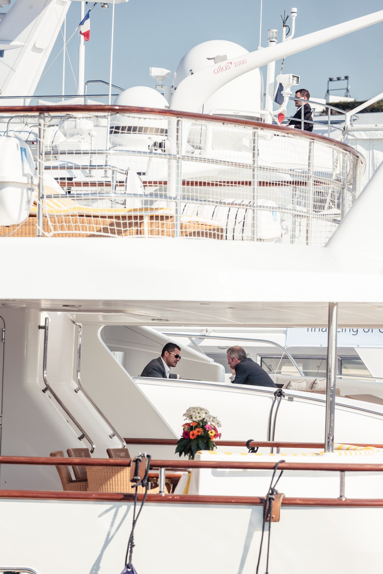 Two men in business attire converse on the deck of a luxury yacht moored in Cannes marina.