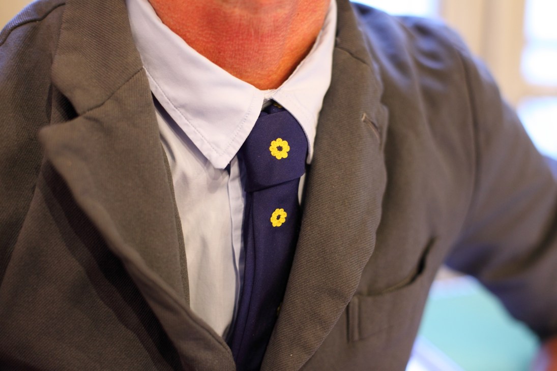 Man wearing a navy tie with yellow flower embroidery, white collar, and grey blazer.