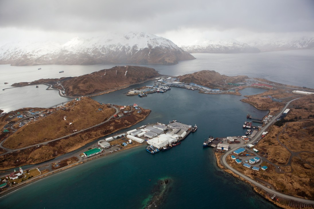 Aerial view of Unalaska and neighbouring Amaknak Island with snow-capped volcanoes and fishing vessels in the harbor.