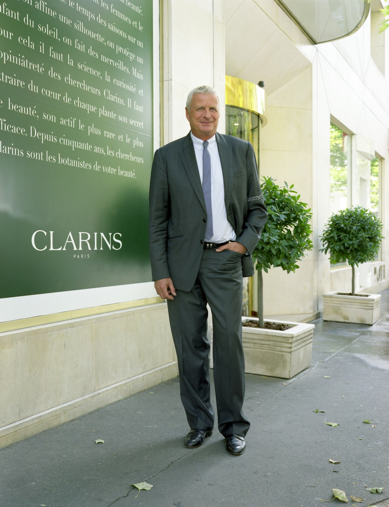 Christian Courtin-Clarins stands outside Clarins Paris headquarters wearing a dark suit and blue tie.