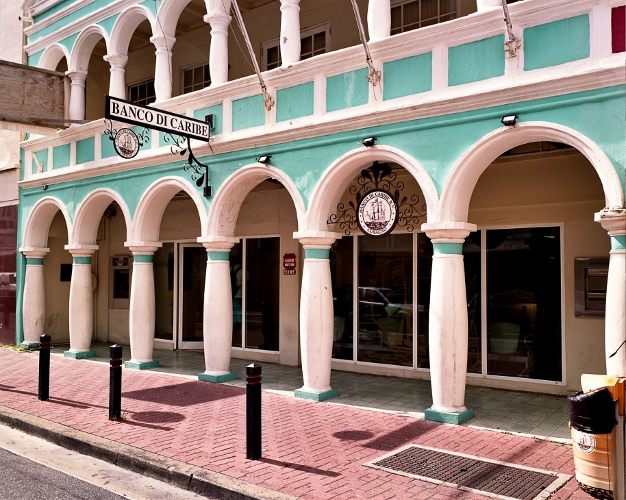 Banco di Caribe storefront with turquoise and pink colonial architecture featuring arched colonnades.