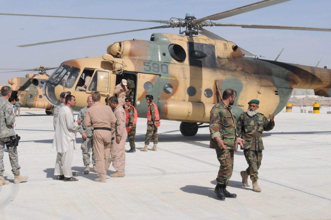 Afghan military personnel stand beside a Mil Mi-8/17 Hip transport helicopter on an airfield.