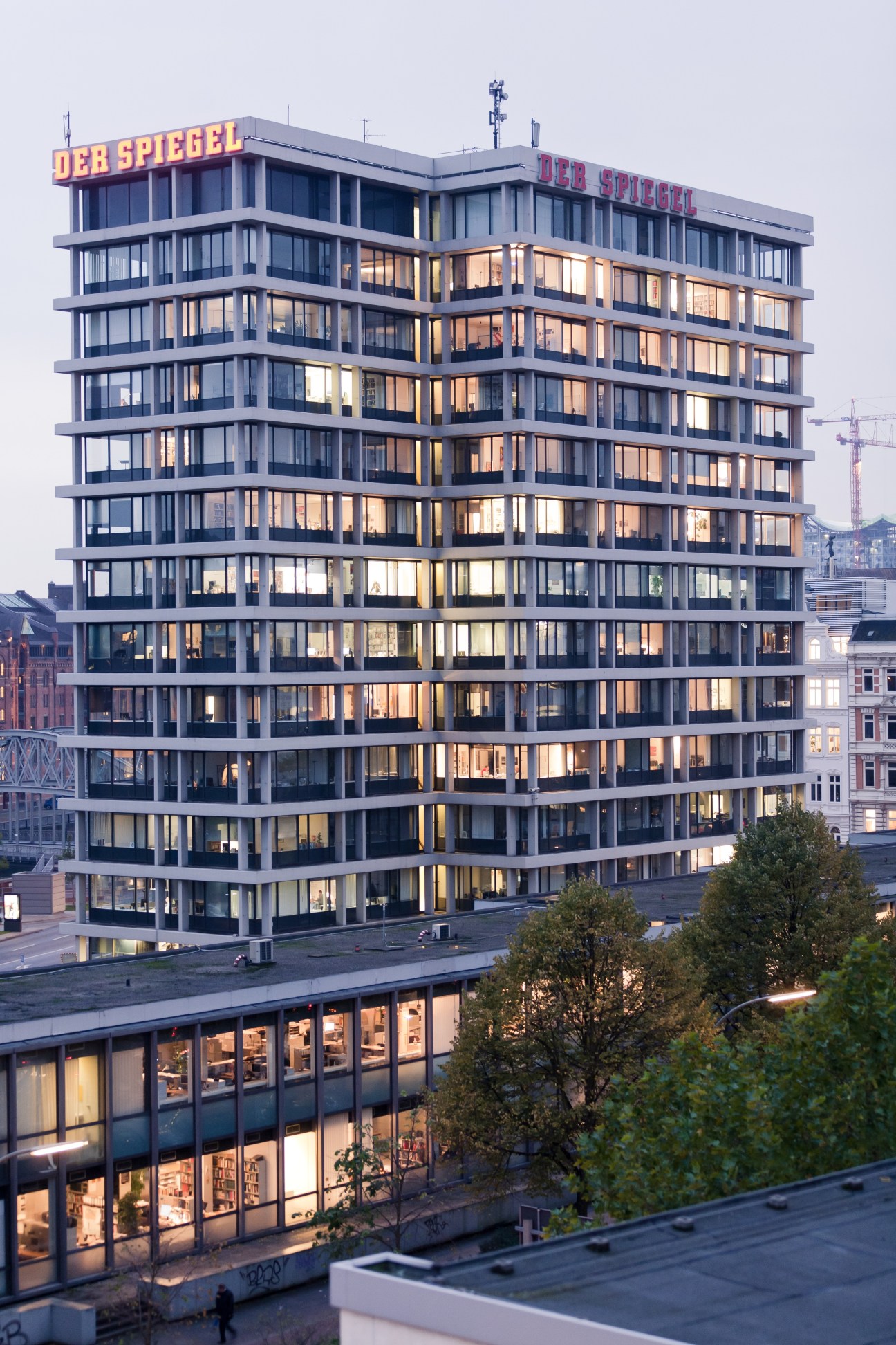 Der Spiegel's mid-century modern headquarters building in Hamburg with illuminated windows and rooftop signage at dusk.