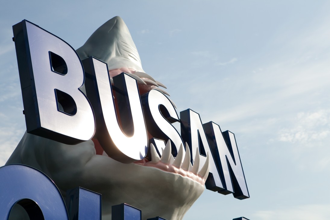 A large shark sculpture sign with illuminated 'BUSAN' lettering at the entrance to Busan Aquarium.