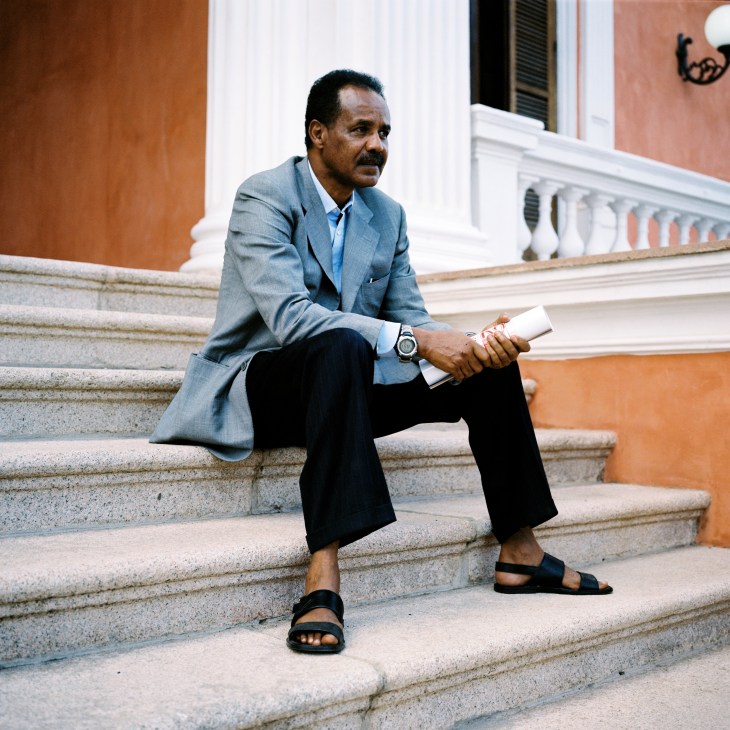 President Isaias Afwerki sits on palace steps in Asmara wearing a grey blazer and holding a document.