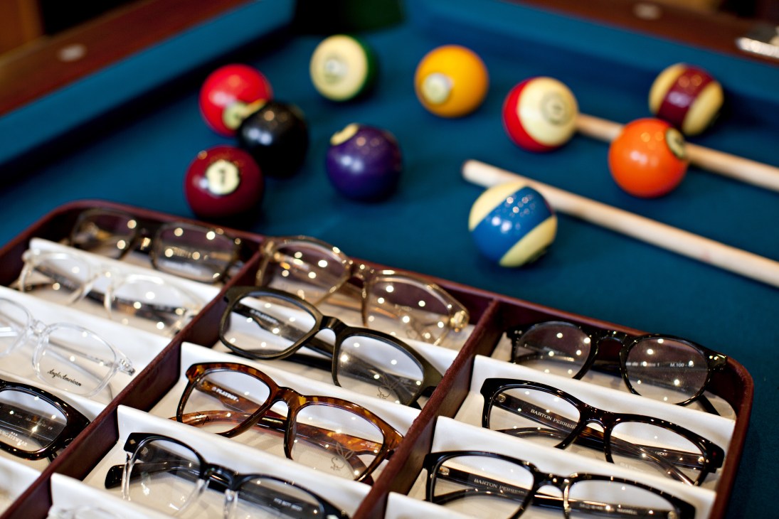 Display of eyeglasses in wooden cases at Silver Lining opticians with a pool table in the background.