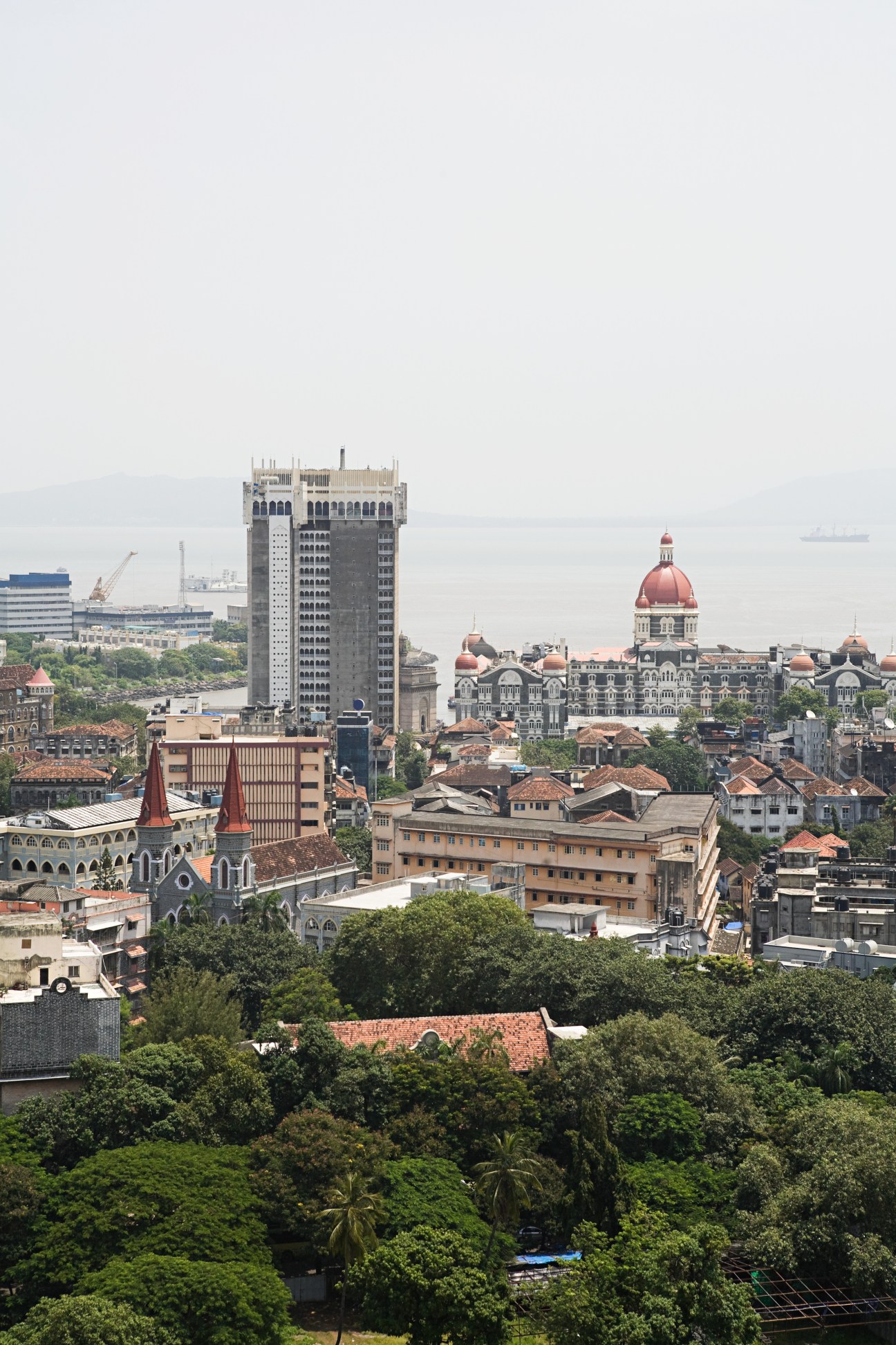 Mumbai skyline showing colonial architecture with red domes, modern high-rises, and the Arabian Sea in the distance.
