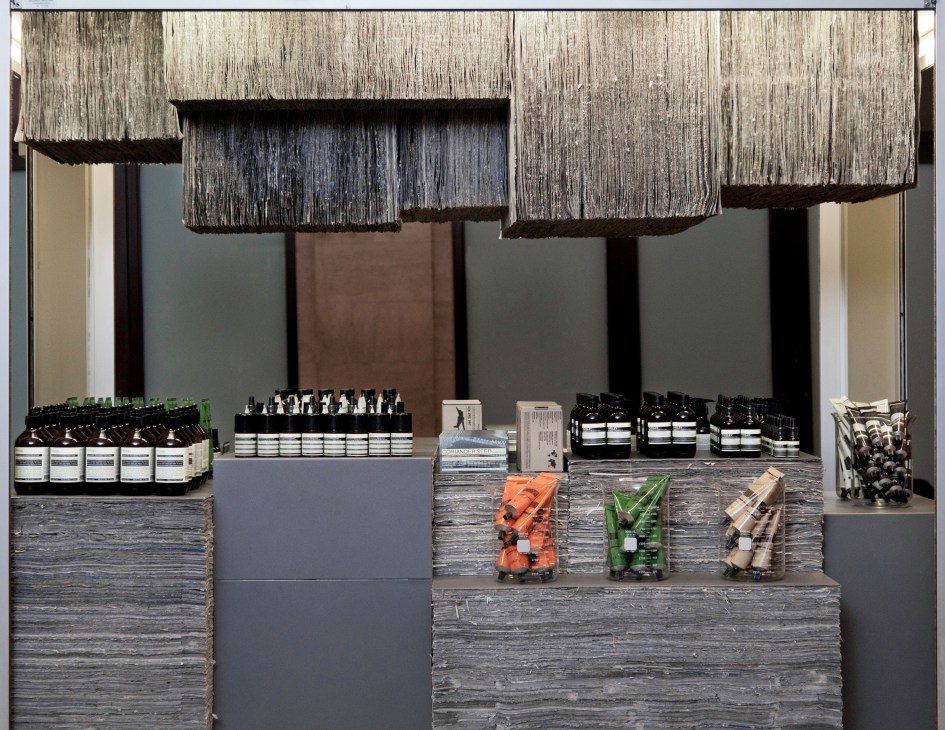 Aesop store interior in New York featuring a counter made from stacked New York Times newspapers with displayed skincare products.