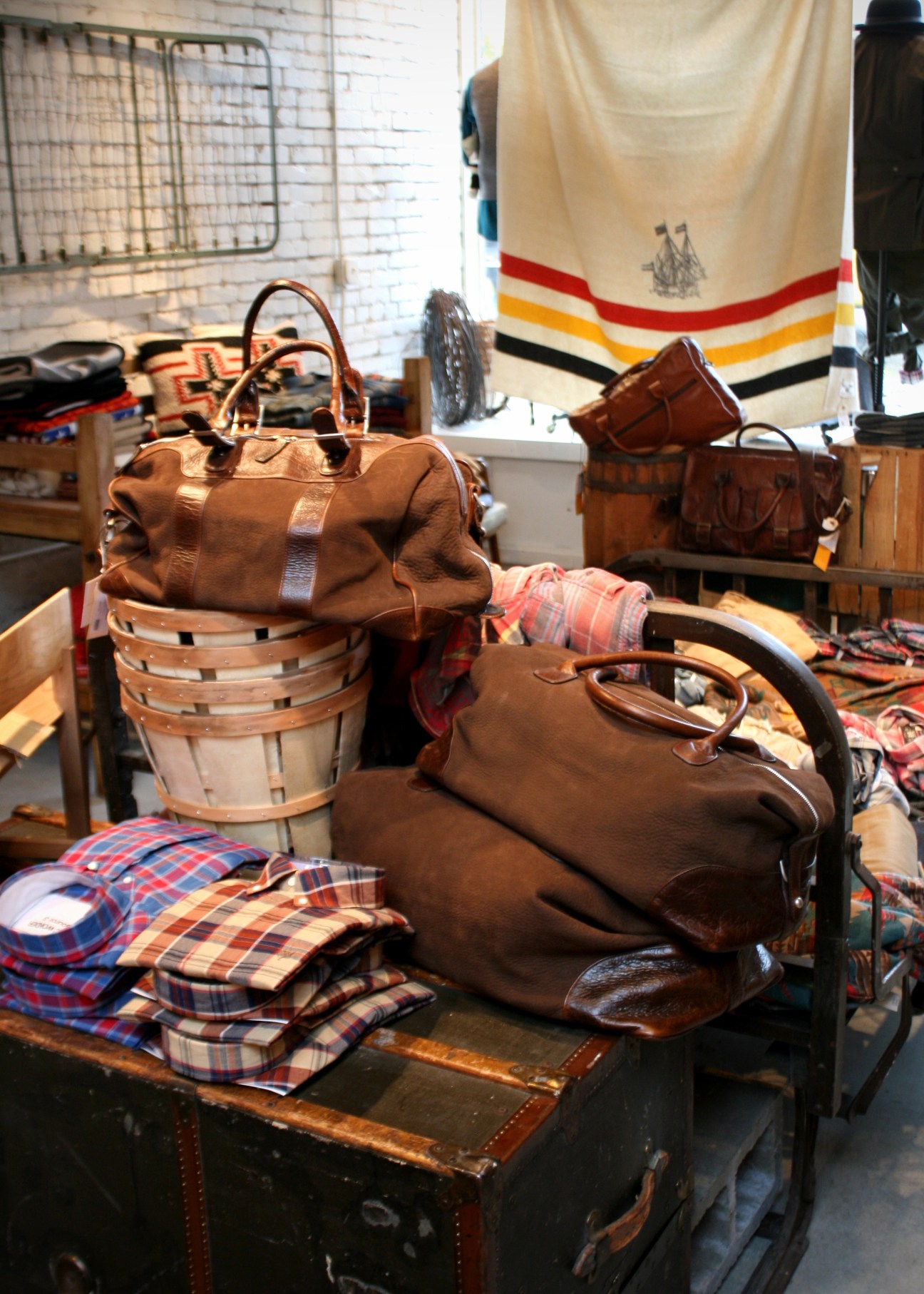 Brown leather bags and plaid fabric displayed on a wooden table in a retail store setting.