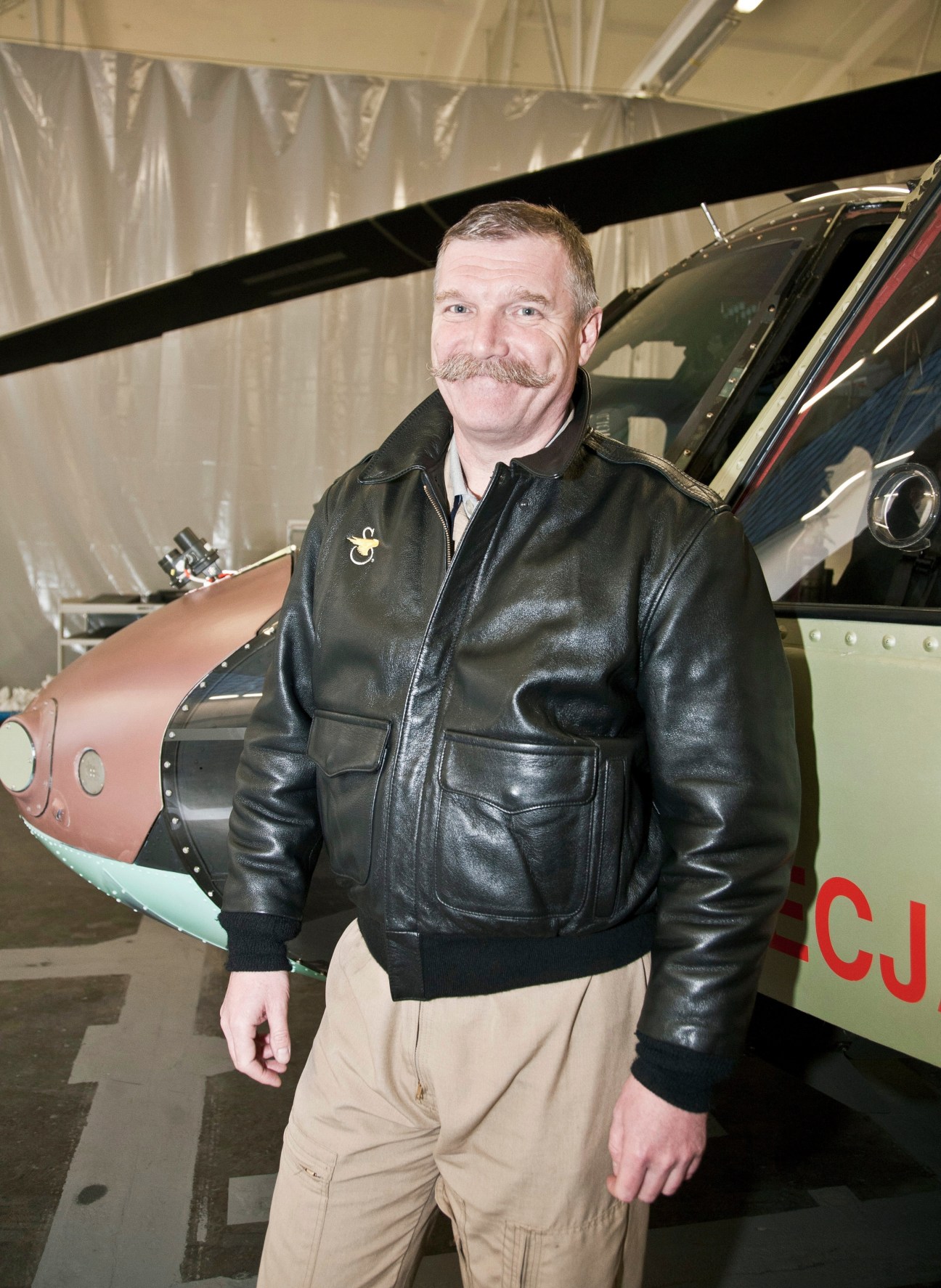 Leszek Pawuła, chief helicopter test pilot, standing in a hangar next to a helicopter.