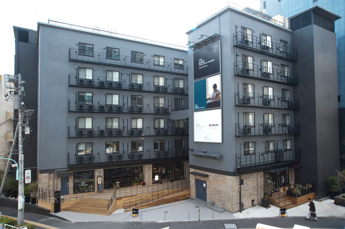 The Share building exterior in Harajuku, a renovated five-story former company dorm with gray façade, brick base, and ground-floor retail spaces.