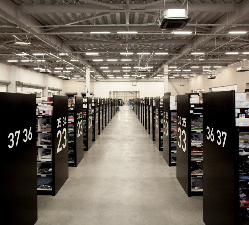 Interior of Zozobase warehouse showing numbered storage cubicles with clothing displayed in a long industrial corridor.
