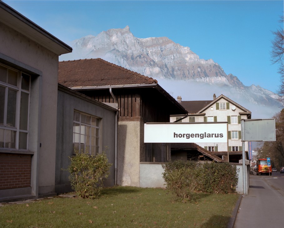 Horgenglarus furniture factory buildings with mountain backdrop in Glarus, Switzerland.