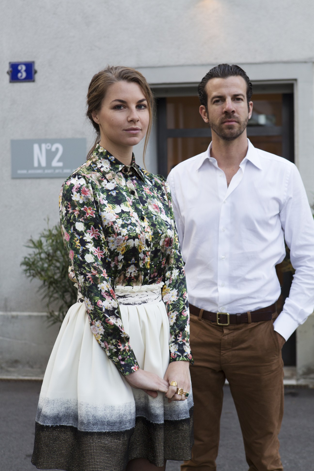 Two people standing outside the N°2 boutique in Zürich, a woman wearing a floral shirt and cream skirt, a man in a white shirt and brown trousers.
