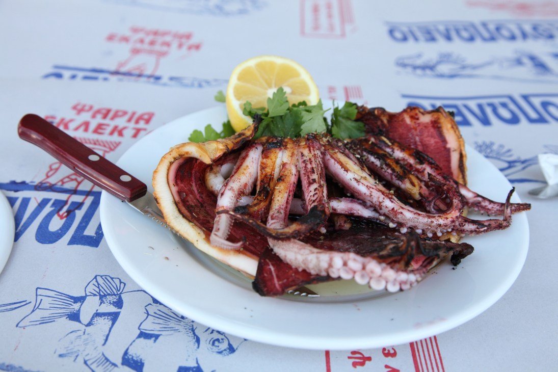 Grilled squid tentacles on a white plate with lemon and parsley at Sardelles restaurant.