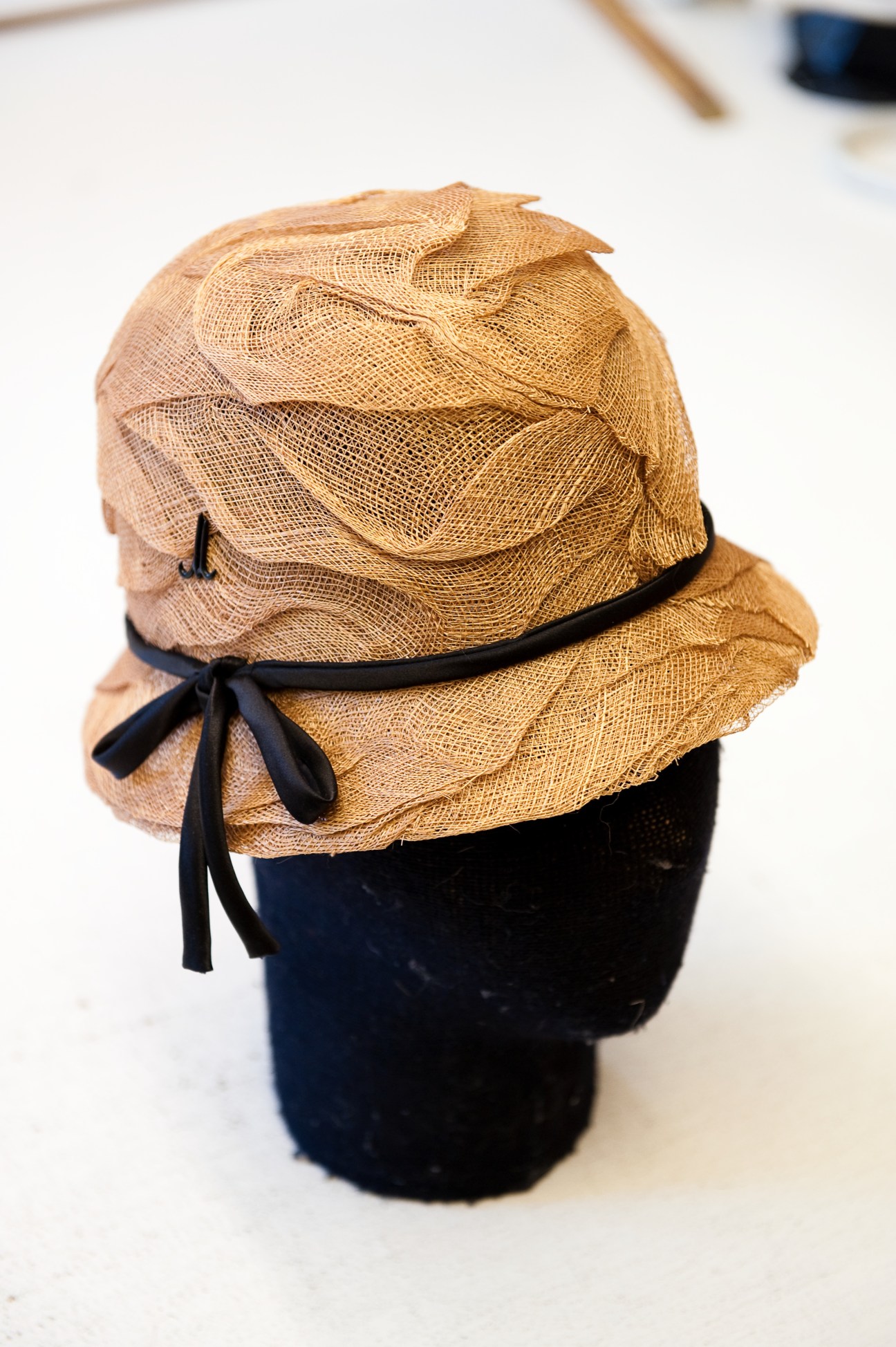 Tan straw hat with black ribbon bow displayed on a dark mannequin head.