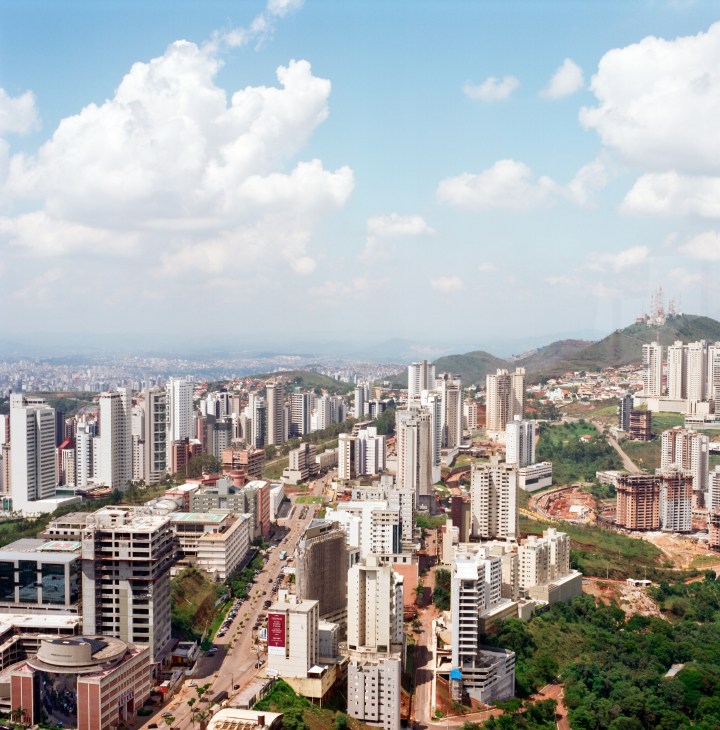 Aerial view of Belo Horizonte's skyline showing modern apartment buildings nestled in hillside valleys under clear blue sky.