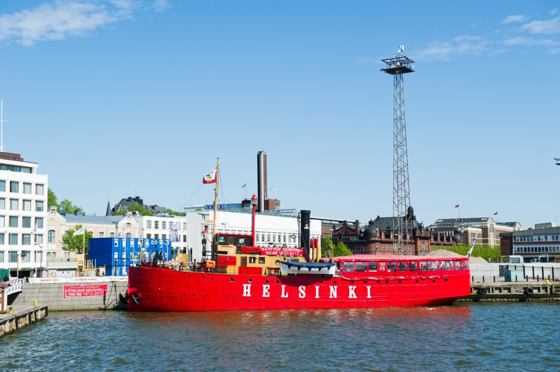 Red icebreaker ship named Helsinki docked at waterfront with modern buildings and tall communications tower in background.